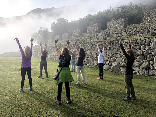 Seven women standing triumphantly with their hands up in the misty mountains of Peru. 