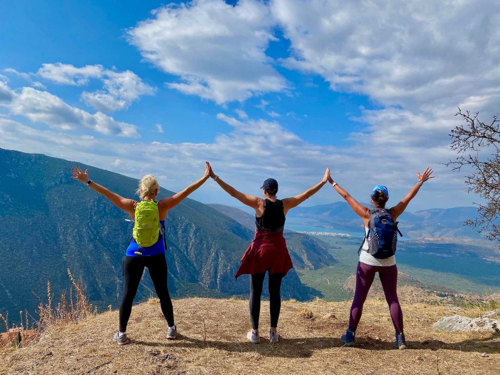 three women standing atop a mountain in greece holding hands