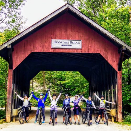 group of women on bikes standing in front of a bridge in Vermont
